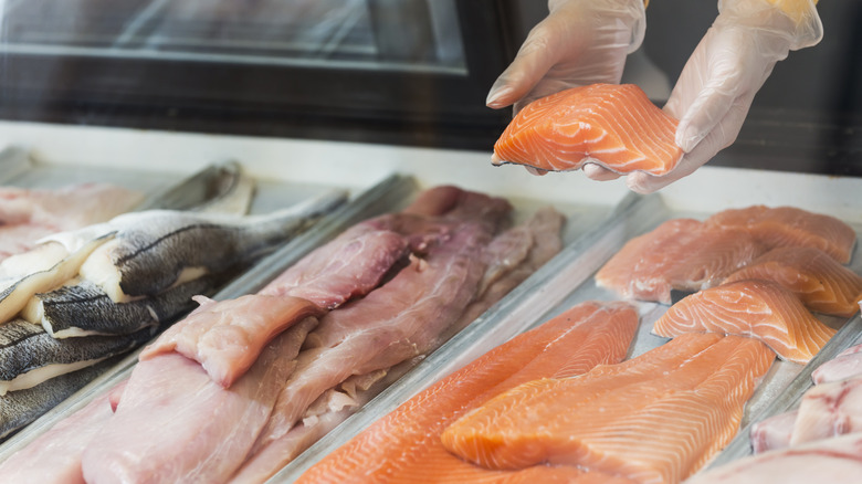 Person removing salmon filet from fish display case