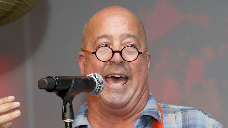 Andrew Zimmern speaking at a mic with his hand raised