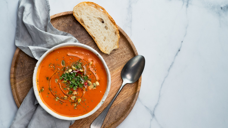 tomato soup with slice of bread on wooden plate with cloth napkin and spoon