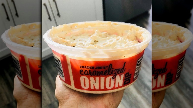 Someone holds a large container of caramelized onion dip from Trader Joe's