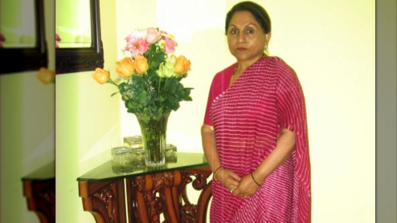 Veena Alfred poses with flower vase wearing a pink sari