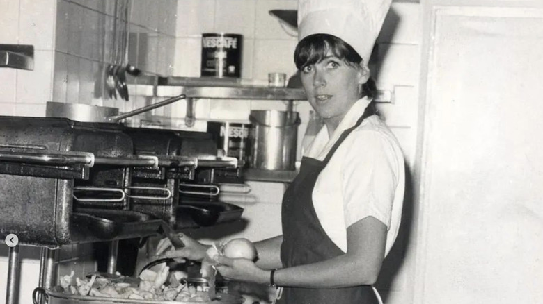 Young Prue Leith in kitchen with chef's hat