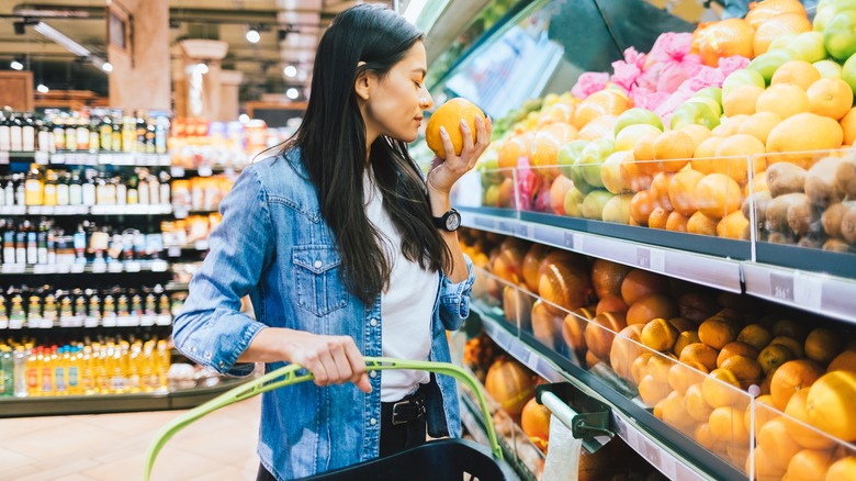 person smelling orange in grocery store