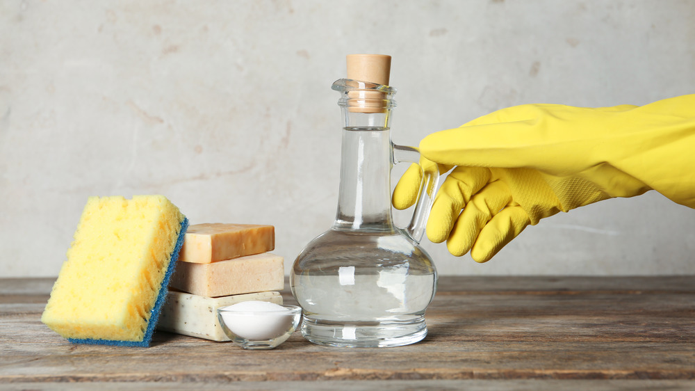 Gloved hand reaching for white vinegar and cleaning supplies