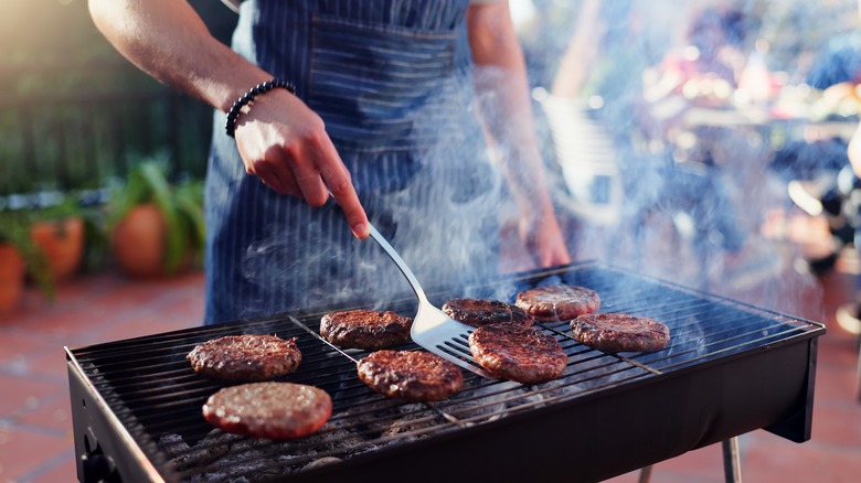 Person grilling burgers with spatula and smoke