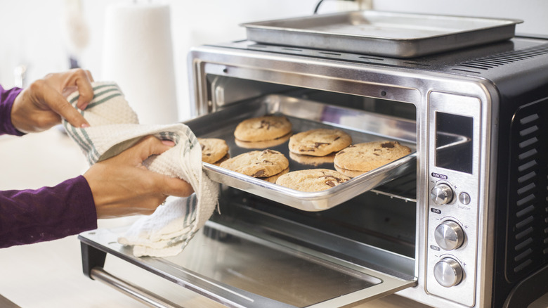 person pulling chocolate chip cookies from toaster oven