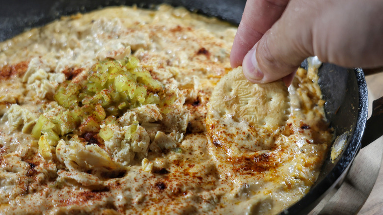 hand dipping cracker into skillet of Nashville hot chicken dip