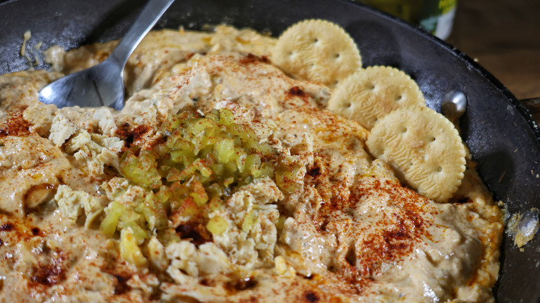 skillet of Nashville hot chicken dip with crackers and chopepd pickles