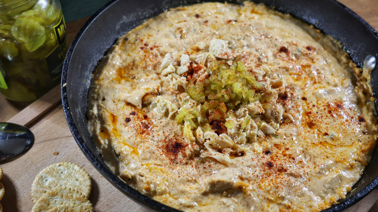 skillet of hot chicken dip garnished with chopped chicken and pickles