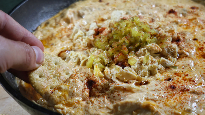 Fingers dipping cracker into skillet of Nashville hot chicken dip