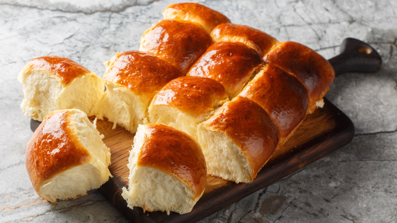 Wooden cutting board holding freshly-baked, fluffy Hawaiian rolls