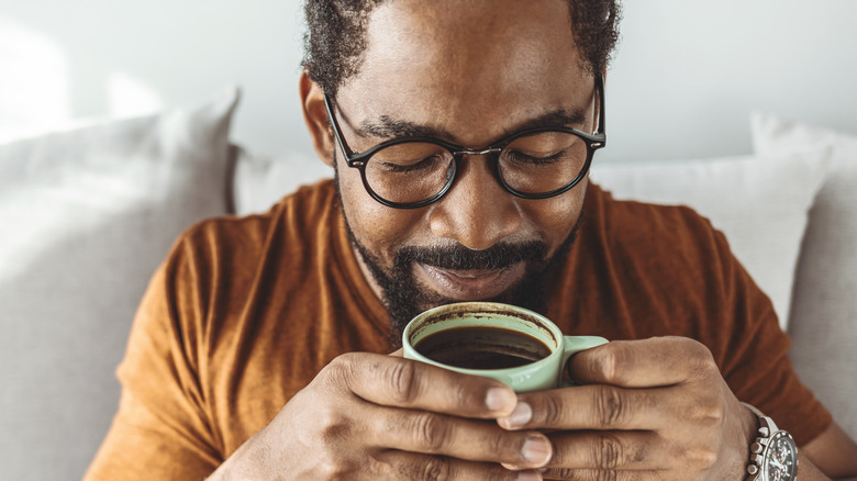 Man with glasses inhaling aroma of cup of coffee. 