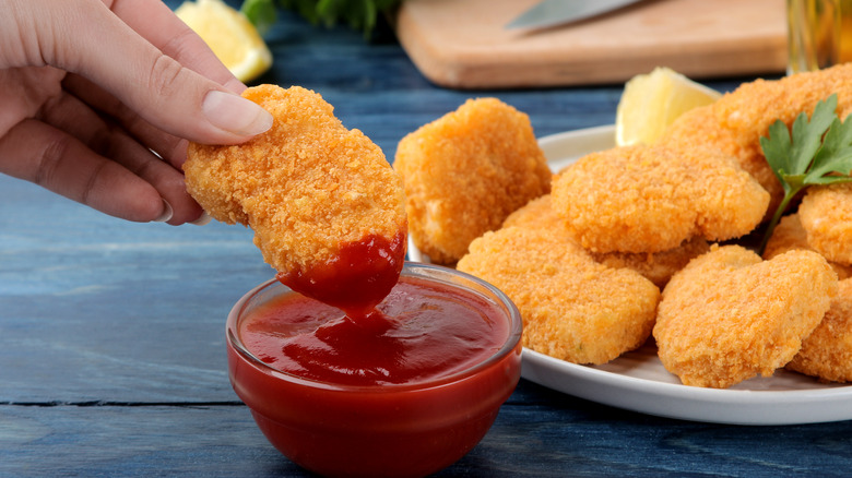 Hand dipping chicken nugget in ketchup