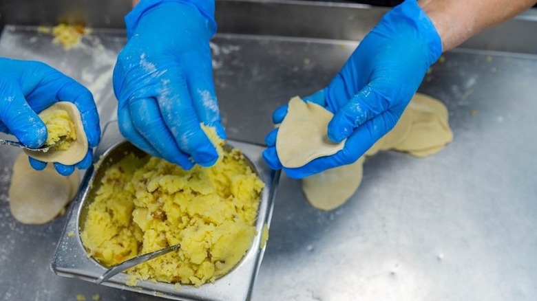 Blue-gloved hands filling pierogis