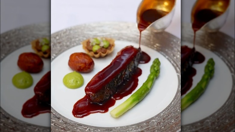 slice of duck with sauce on it, more condiments on side with one asparagus spear