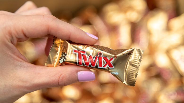 A woman holding up a fun-sized Twix candy bar 