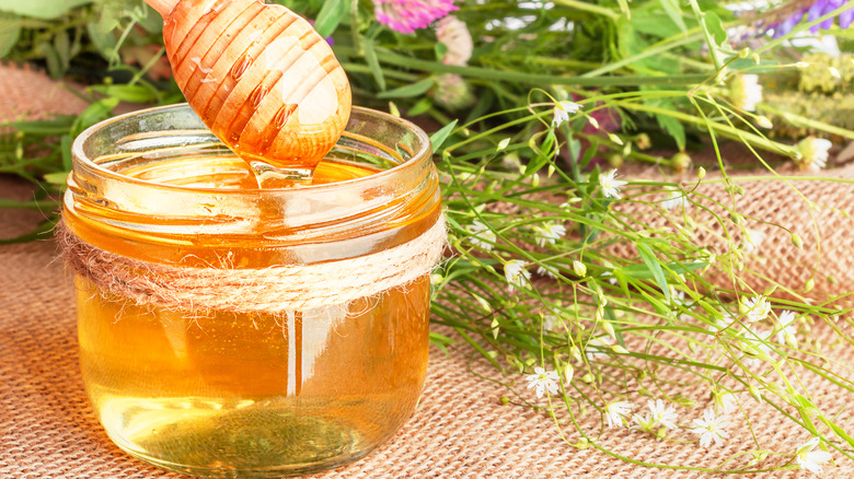 jar of honey and dipper with wildflowers