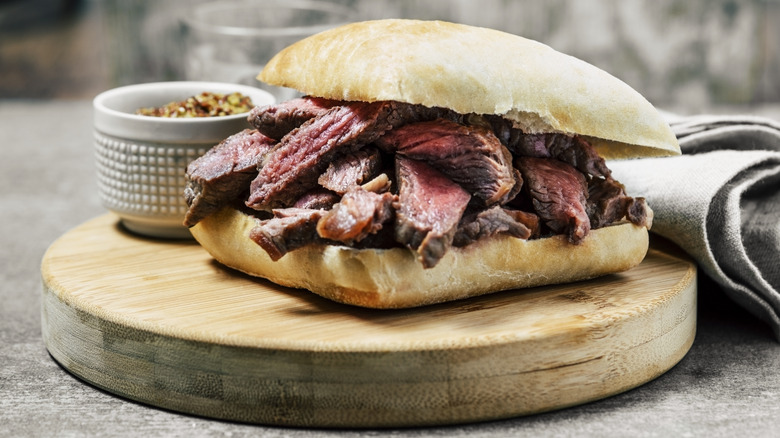 Steak sandwich on ciabatta bread on wooden cutting board