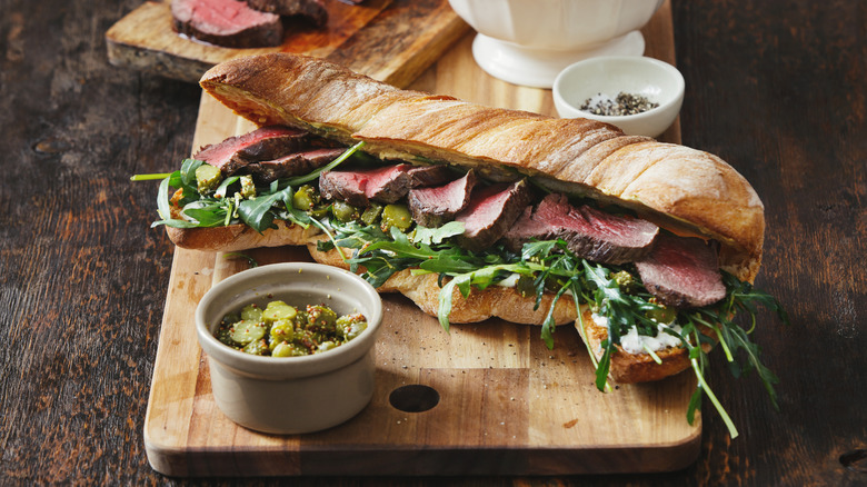 Steak sandwich on wood cutting board with various toppings