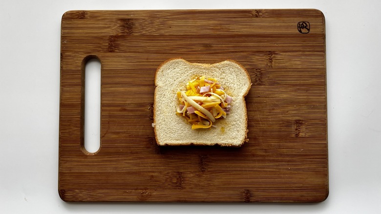 bread with jelly, chopped ham, and shredded cheese on a wooden board