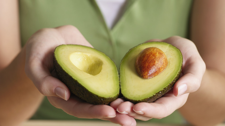 hands holding a split avocado