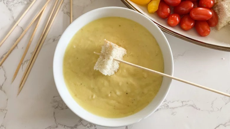 Skewer with bread being dipped into cheese fondue