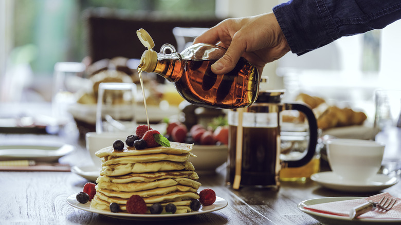 hand pouring syrup on pancakes