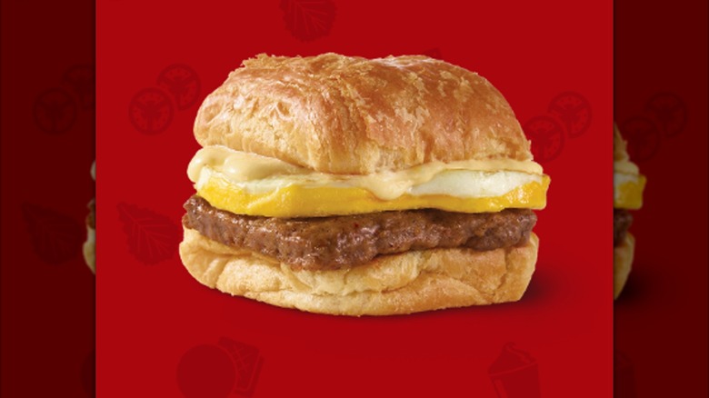 A sausage croissant with eggs and cheese from Wendy's is shown on a red background.