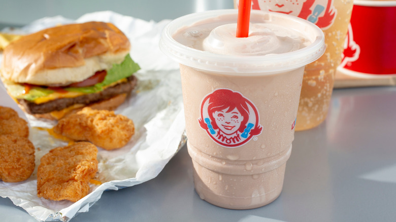 A Wendy's Frosty accompanies a burger and chicken pieces on a table.