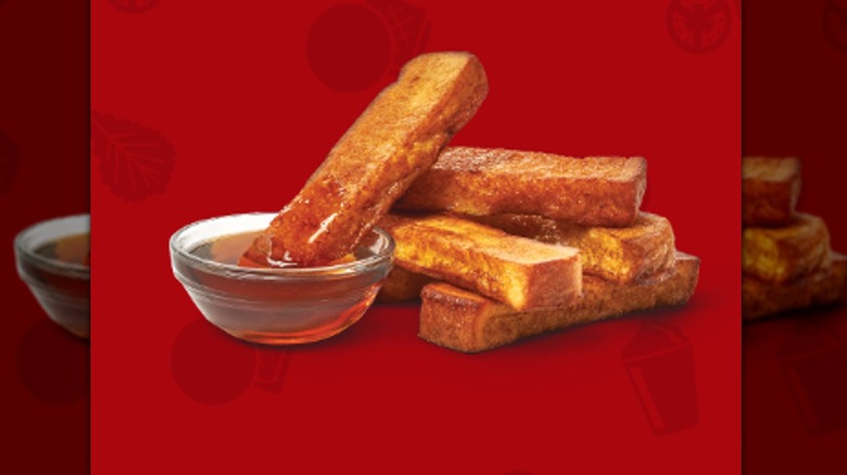 French toast sticks from Wendy's with syrup are on a red background.