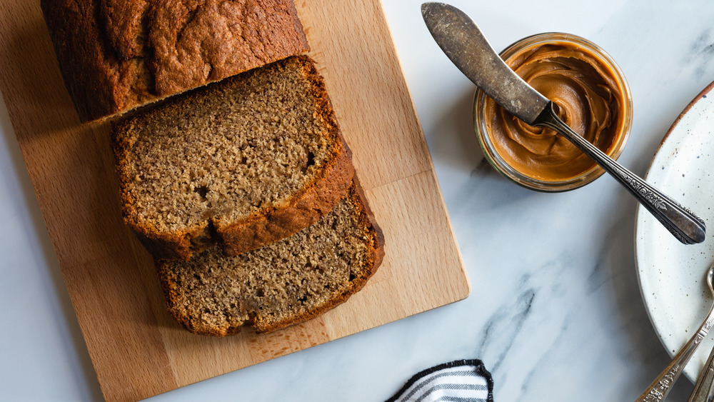 sliced loaf of  cookie butter banana bread on a wooden cutting board by a jar of cookie butter