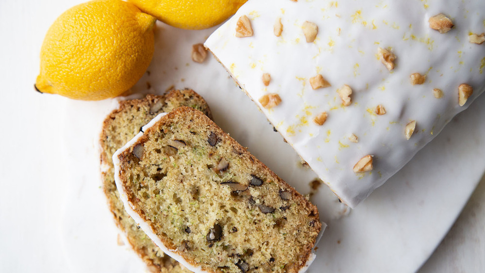 sliced zucchini walnut bread with lemon glaze on a white counter near lemons