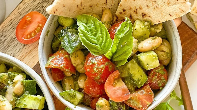 Bowls of pesto coated beans, tomatoes, and cucumber