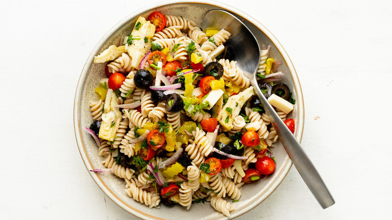 Bowl of cooked pasta with olives, onion, tomato, and peppers