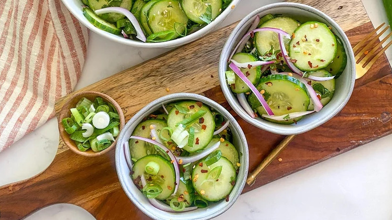 Bowls of sliced cucumbers with red onion, scallions, and chile flakes.