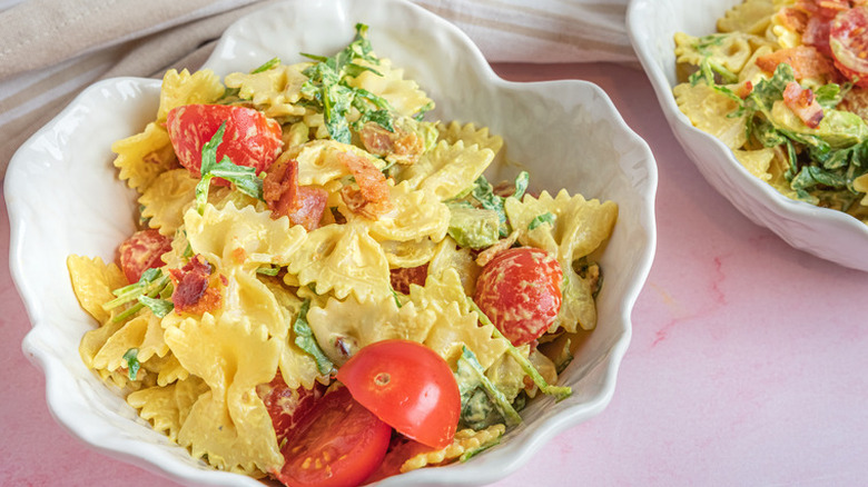 White bowl of pasta salad with tomatoes and herbs.