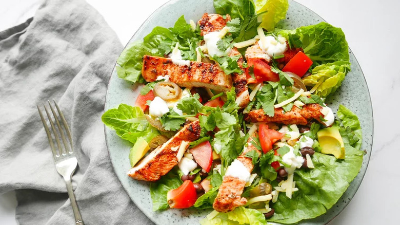 Gray plate with green salad, seasoned chicken strips, and dressing