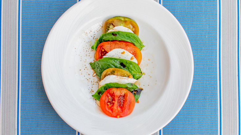 White plate with slices of tomato, mozzarella, and basil leaves