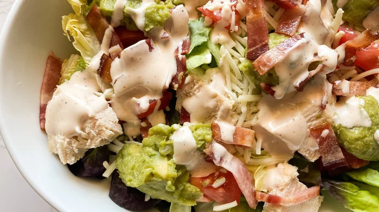 Salad with avocado, chicken, bacon, dressing, and lettuce