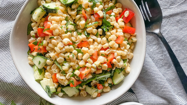 Corn kernels, peppers, cucumbers, and herbs combined in a bowl