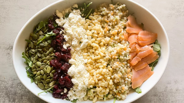 Oval dish with rows of corn, cranberries, salmon, and couscous