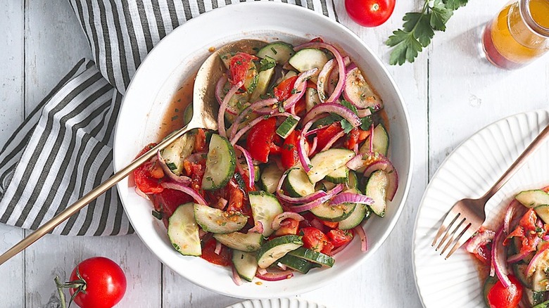 White bowl of chopped tomato and cucumber salad with fork.