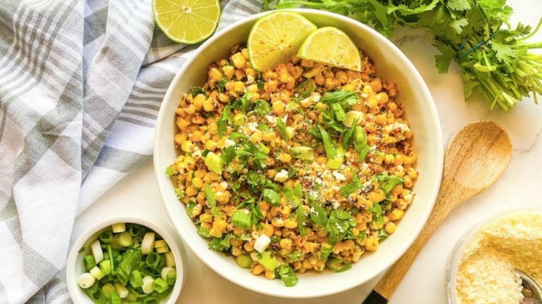 White bowl with corn kernel salad, with limes and spices.