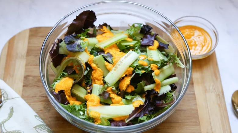 Glass bowl of cucumber-topped salad with orange dressing.