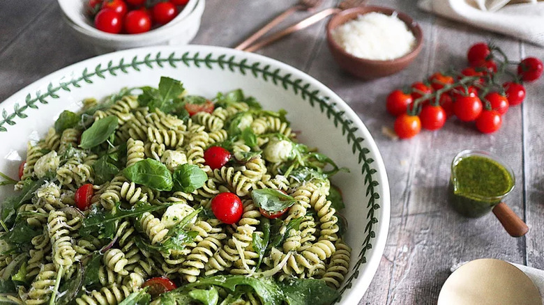 Large bowl of rotini pasta with pesto, tomatoes, and arugula.