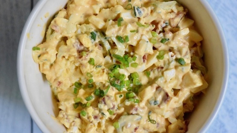 Bowl of creamy egg salad with sliced scallions.