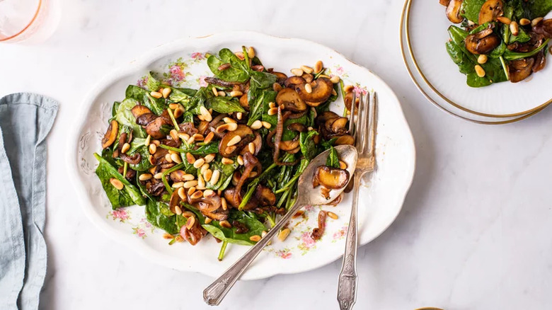 White plate with spinach, pine nuts, and mushrooms