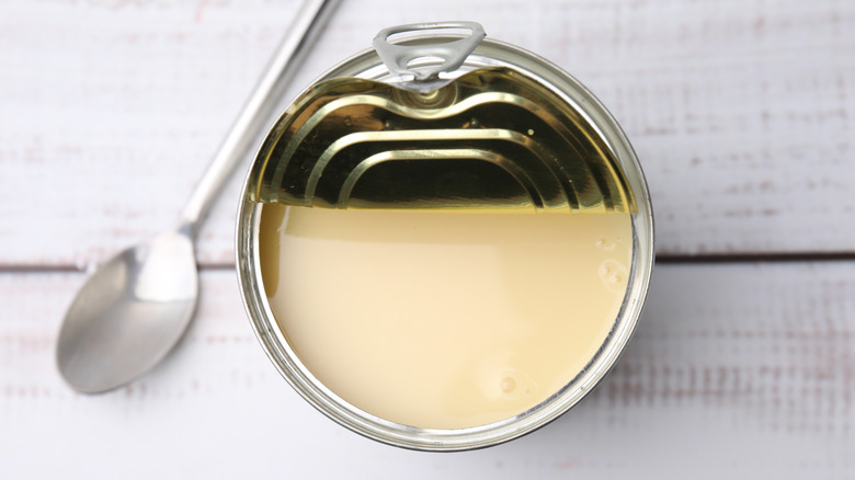 Open can of condensed milk next to a spoon