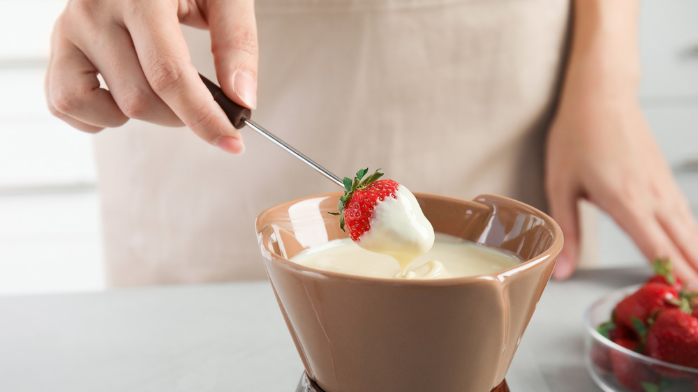 Woman dips strawberry in white chocolate