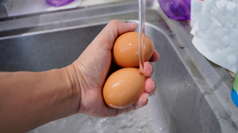 Hand holding two eggs under running water